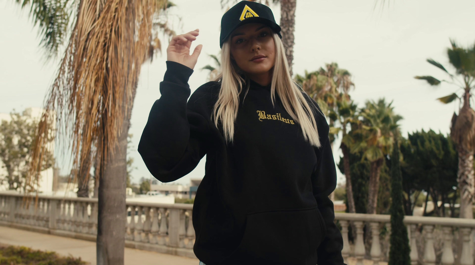 a woman in a black hoodie is standing by a palm tree