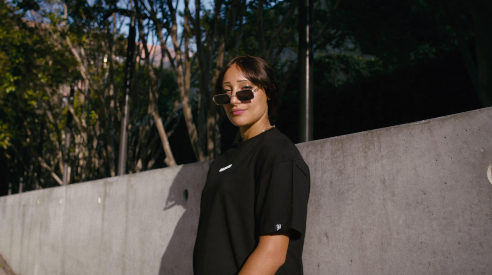 a woman in a black shirt and sunglasses leaning against a wall