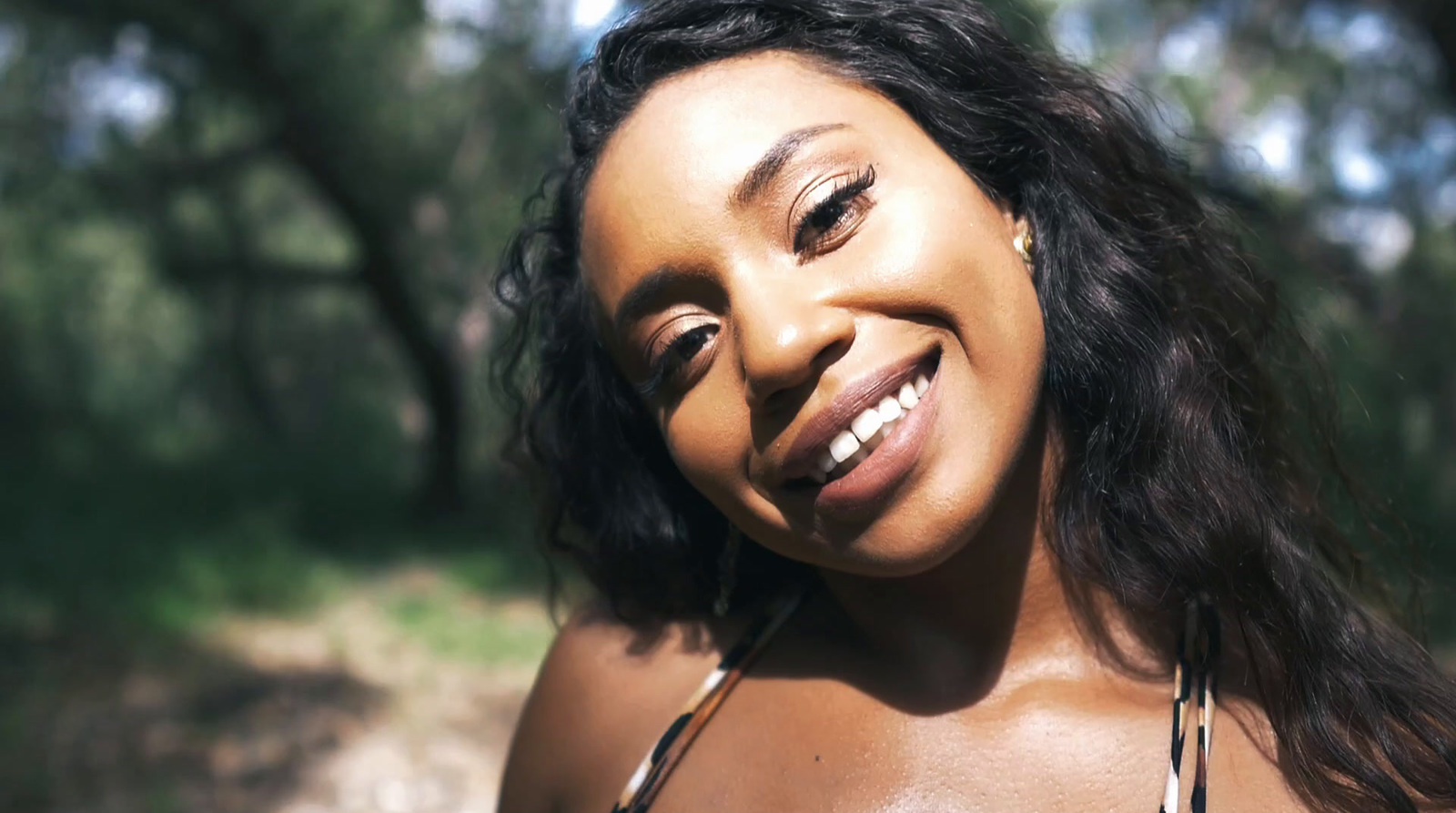 a close up of a woman smiling with trees in the background