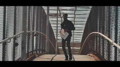 a man walking across a bridge holding a surfboard