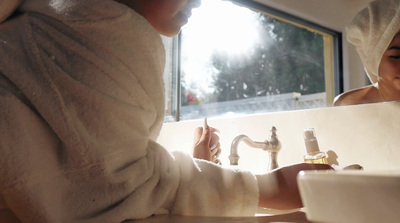 a woman in a bathrobe washing her hands in a sink