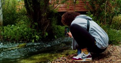 a person kneeling down taking a picture of a stream