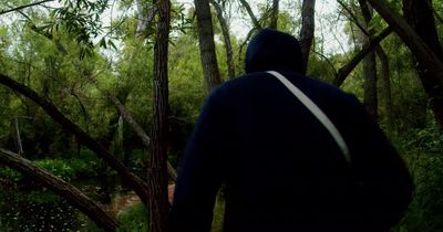 a man in a hooded jacket walking through a forest