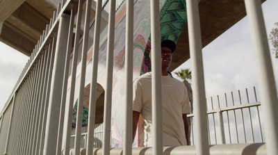 a man standing behind a fence holding a skateboard