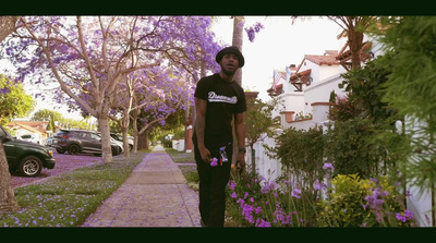 a man standing on a sidewalk next to purple flowers