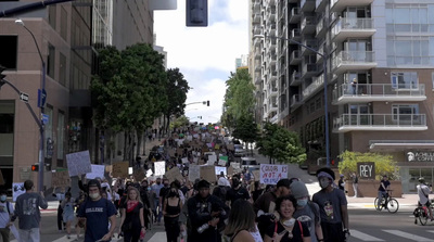 a crowd of people walking down a street next to tall buildings