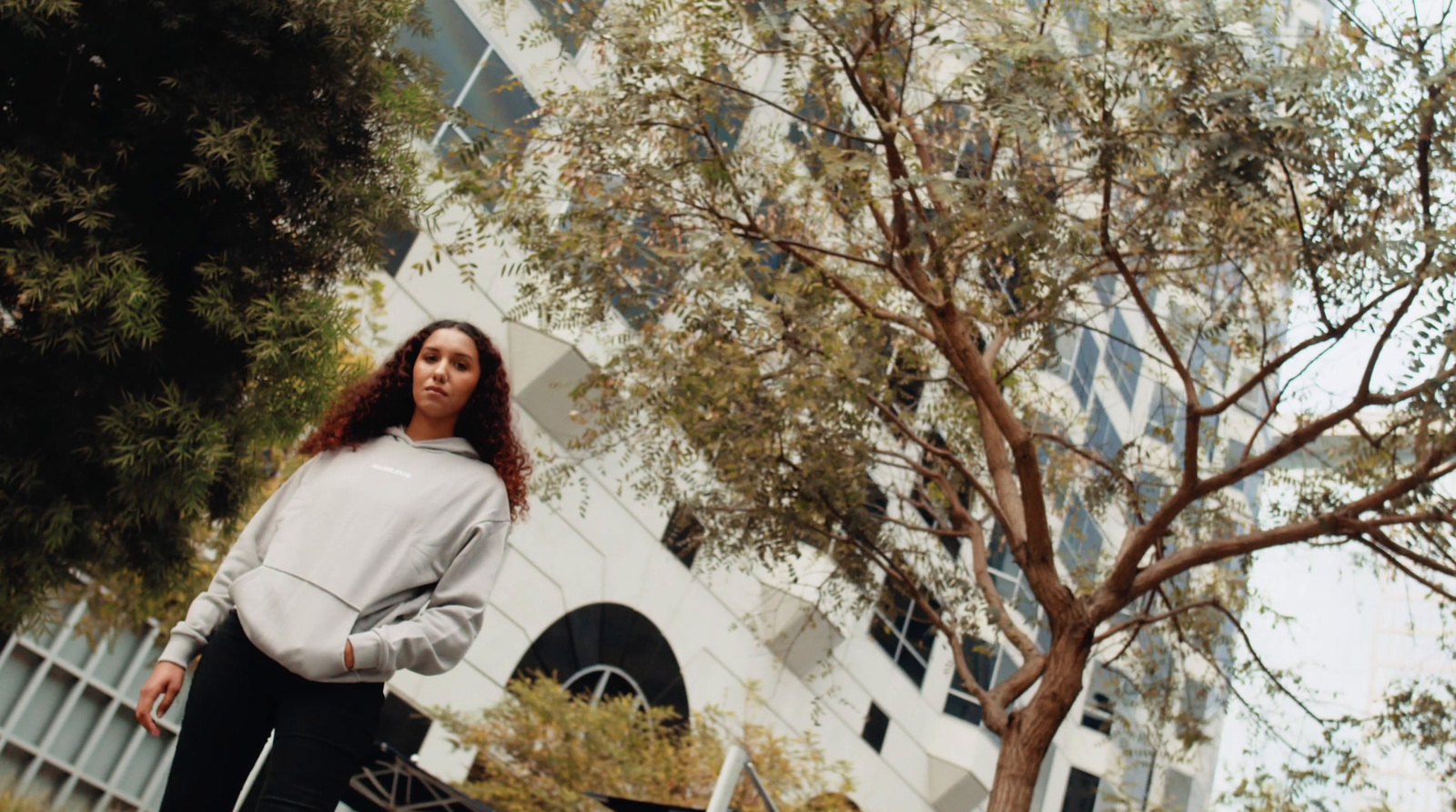 a woman standing next to a tree in front of a building