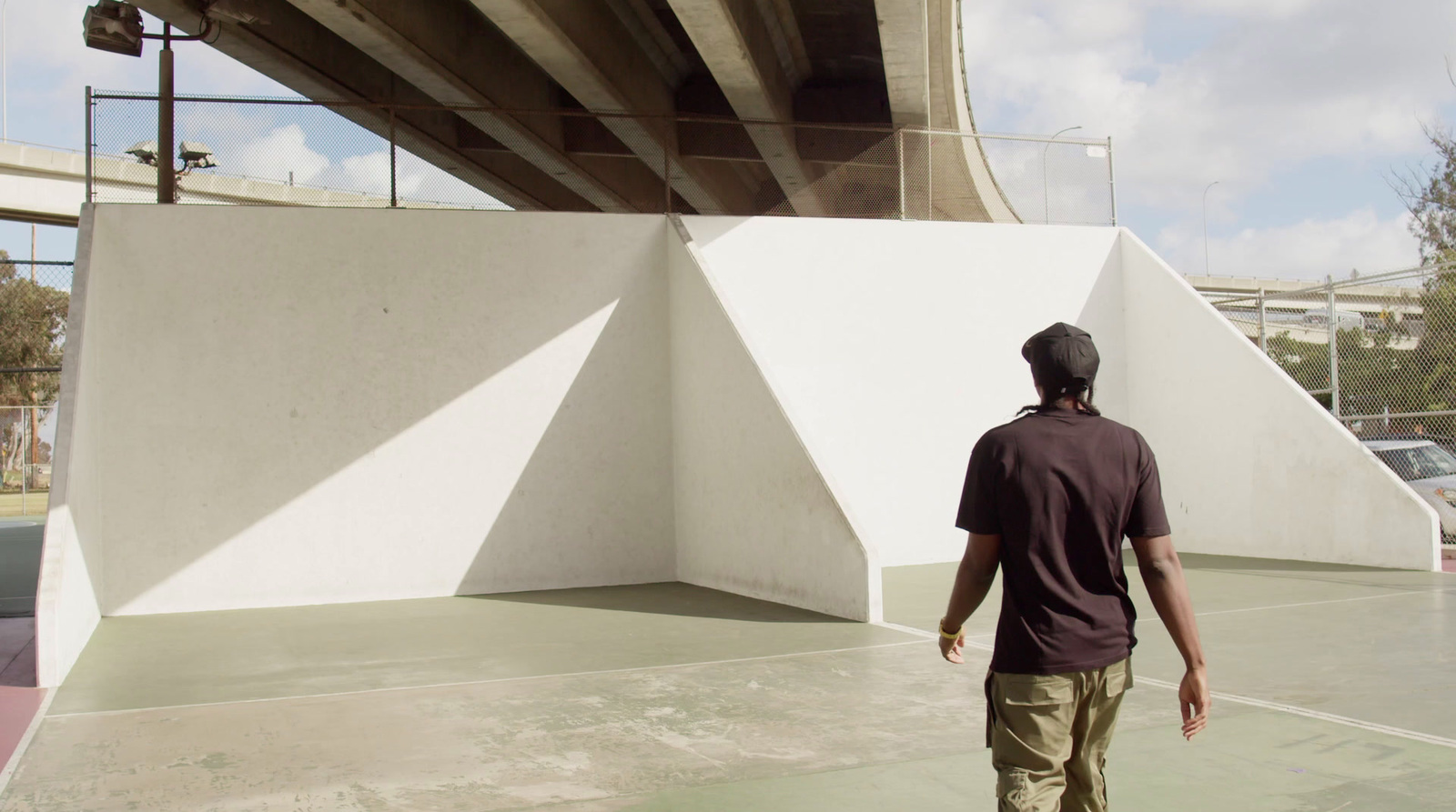 a man walking under a bridge with a skateboard