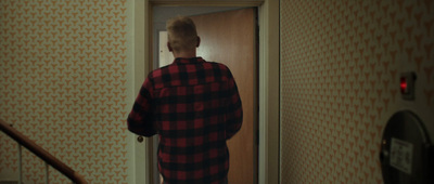 a man in a red and black flannel shirt standing in a doorway