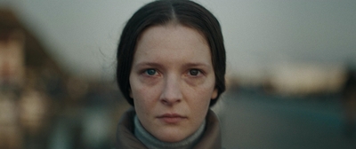 a woman in a gray jacket is staring at the camera