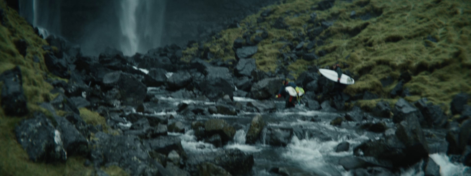 a couple of people with surfboards near a waterfall