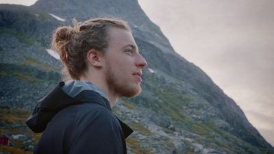 a man in a black jacket standing in front of a mountain