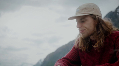 a man with long hair and a hat sitting on a rock