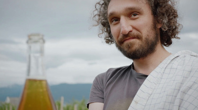 a man with curly hair standing next to a bottle of beer