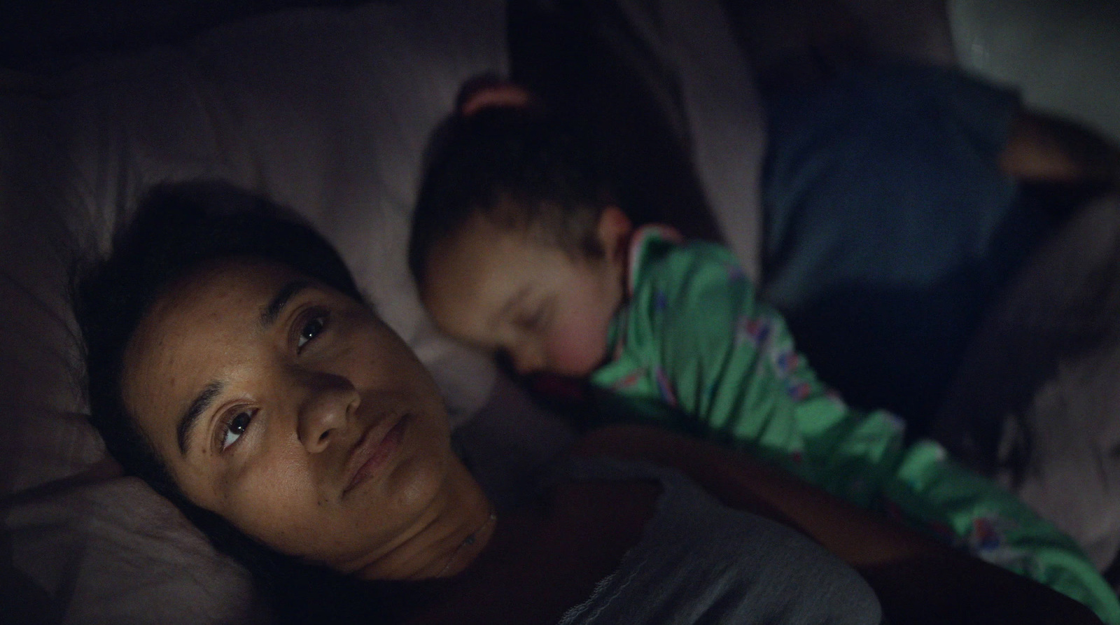 a woman and a child laying in bed at night