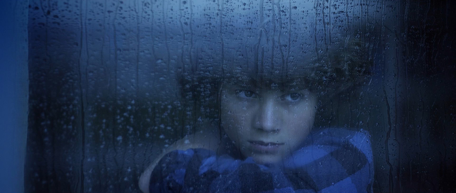 a boy looking out of a window with rain drops on it