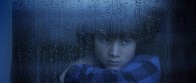 a boy looking out of a window with rain drops on it