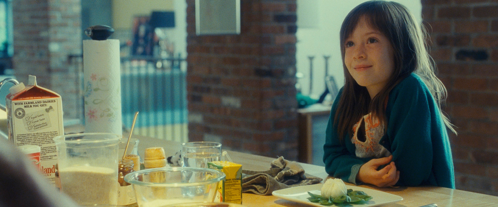 a young girl sitting at a table with food in front of her