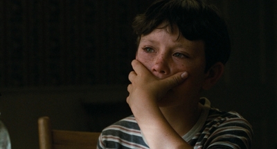 a boy is sitting at a table with his hand on his face