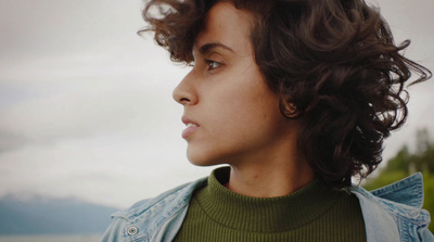 a young woman with curly hair is staring off into the distance