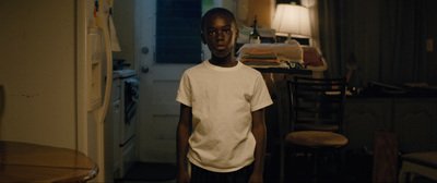 a young boy in a white t - shirt standing in a kitchen