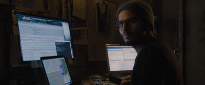 a man in a beanie in front of two monitors