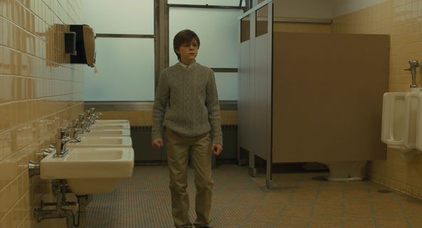 a boy standing in a bathroom with sinks and urinals