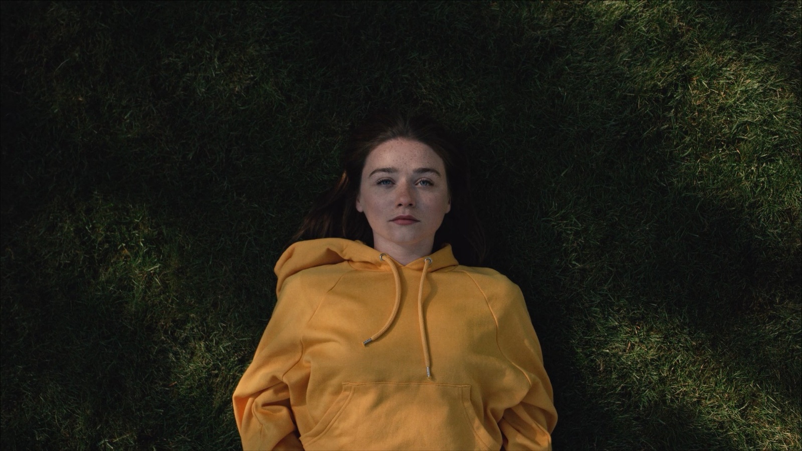 a girl laying on the grass in a yellow hoodie