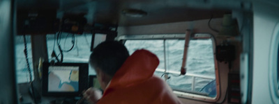 a man in an orange jacket is looking at a monitor on a boat