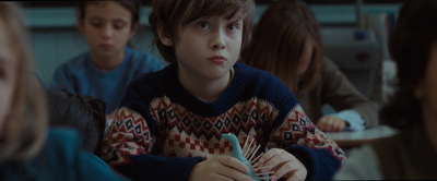 a boy is sitting in a classroom with other children