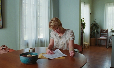 a woman sits at a table and writes on a piece of paper