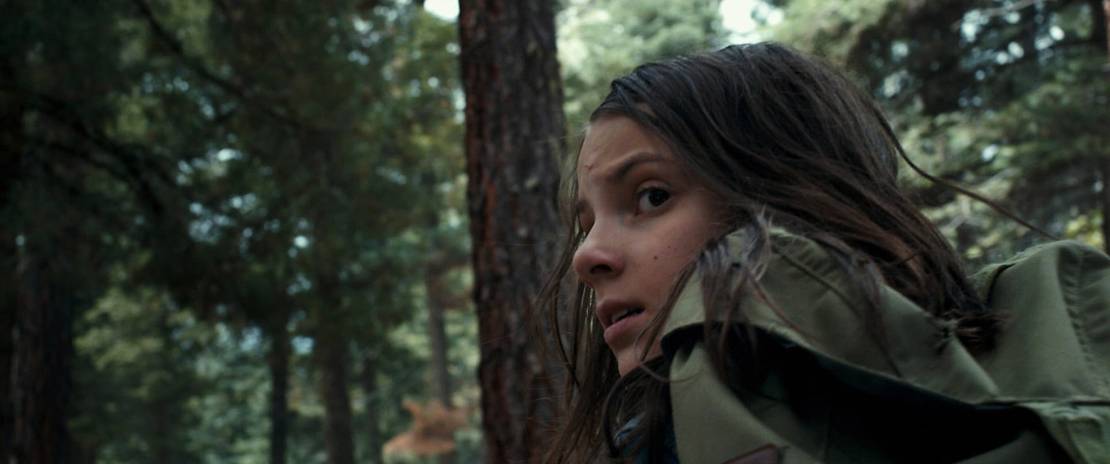 a girl in a green jacket standing in a wooded area