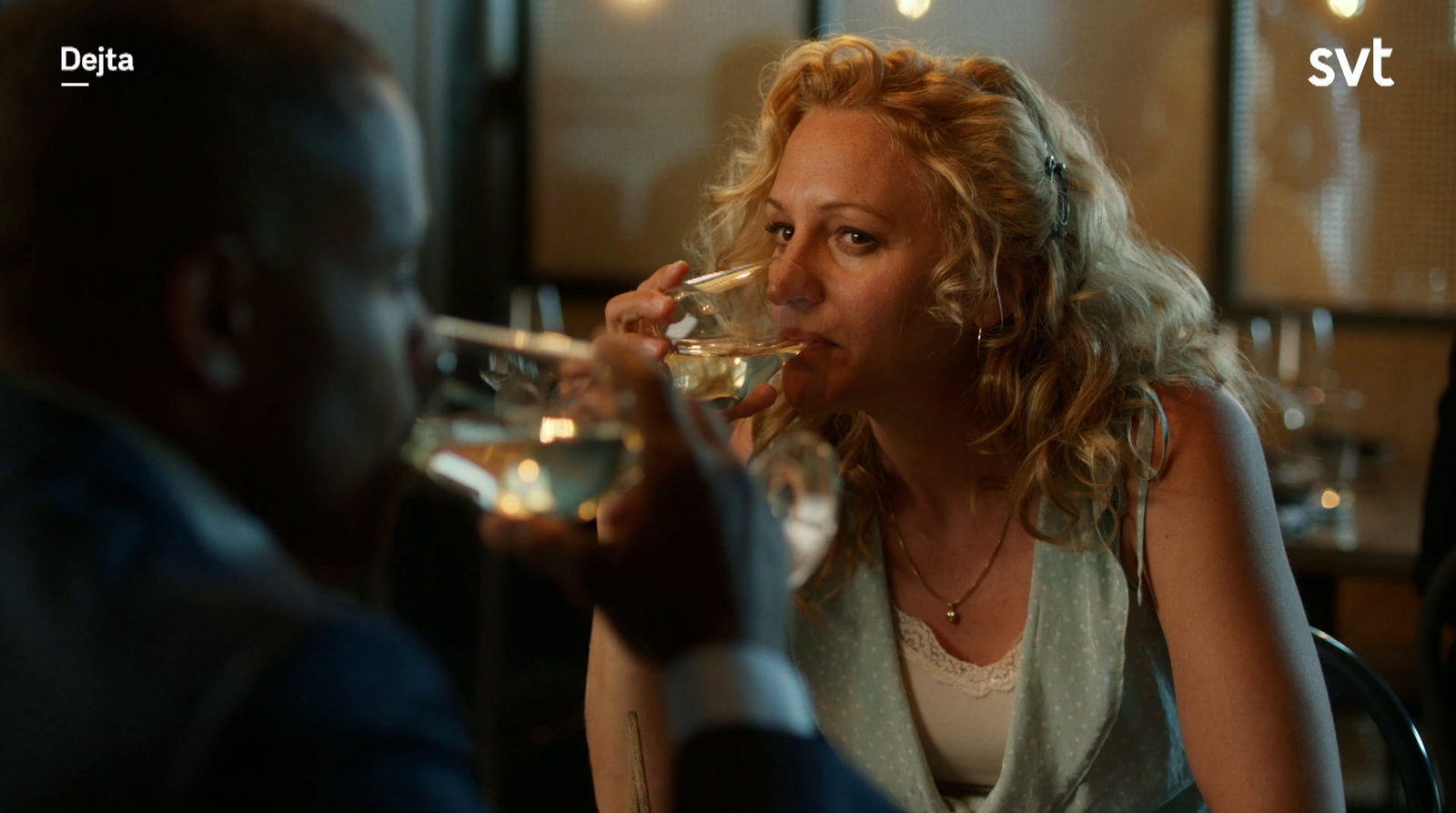 a woman drinking from a wine glass next to a man