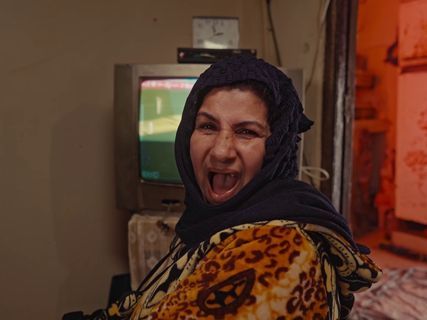 a woman wearing a headscarf is laughing in front of a television