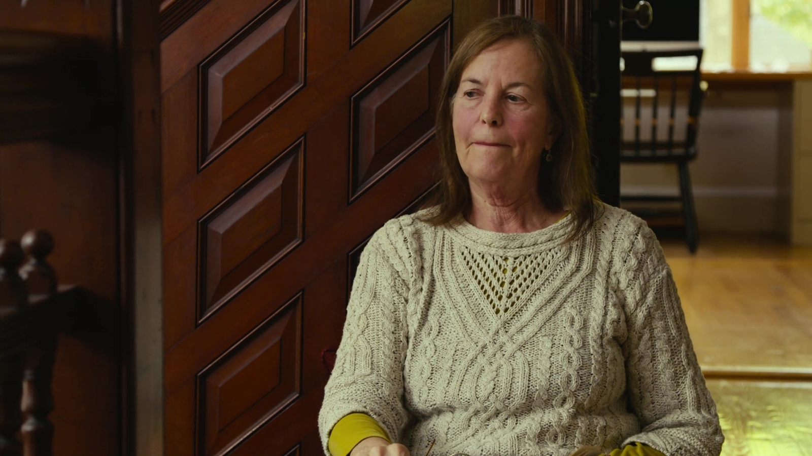 a woman in a sweater sits on a wooden floor