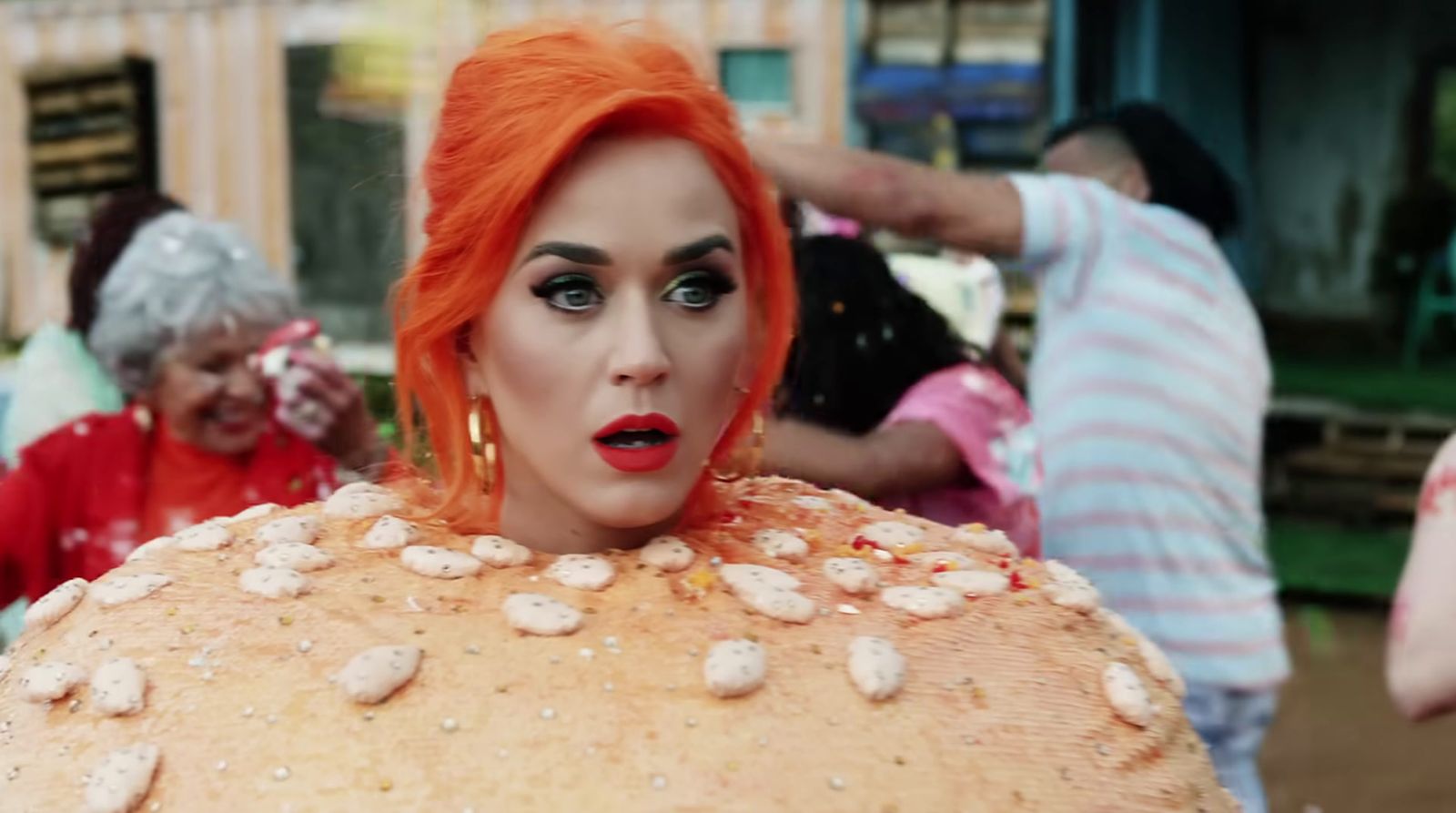 a woman with orange hair and makeup is standing in front of a group of people