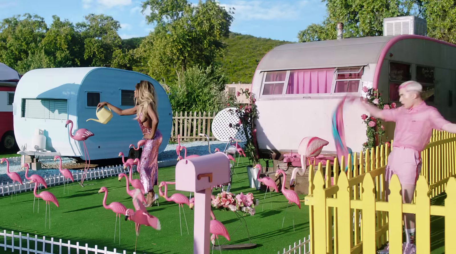 a couple of pink flamingos standing next to a yellow fence