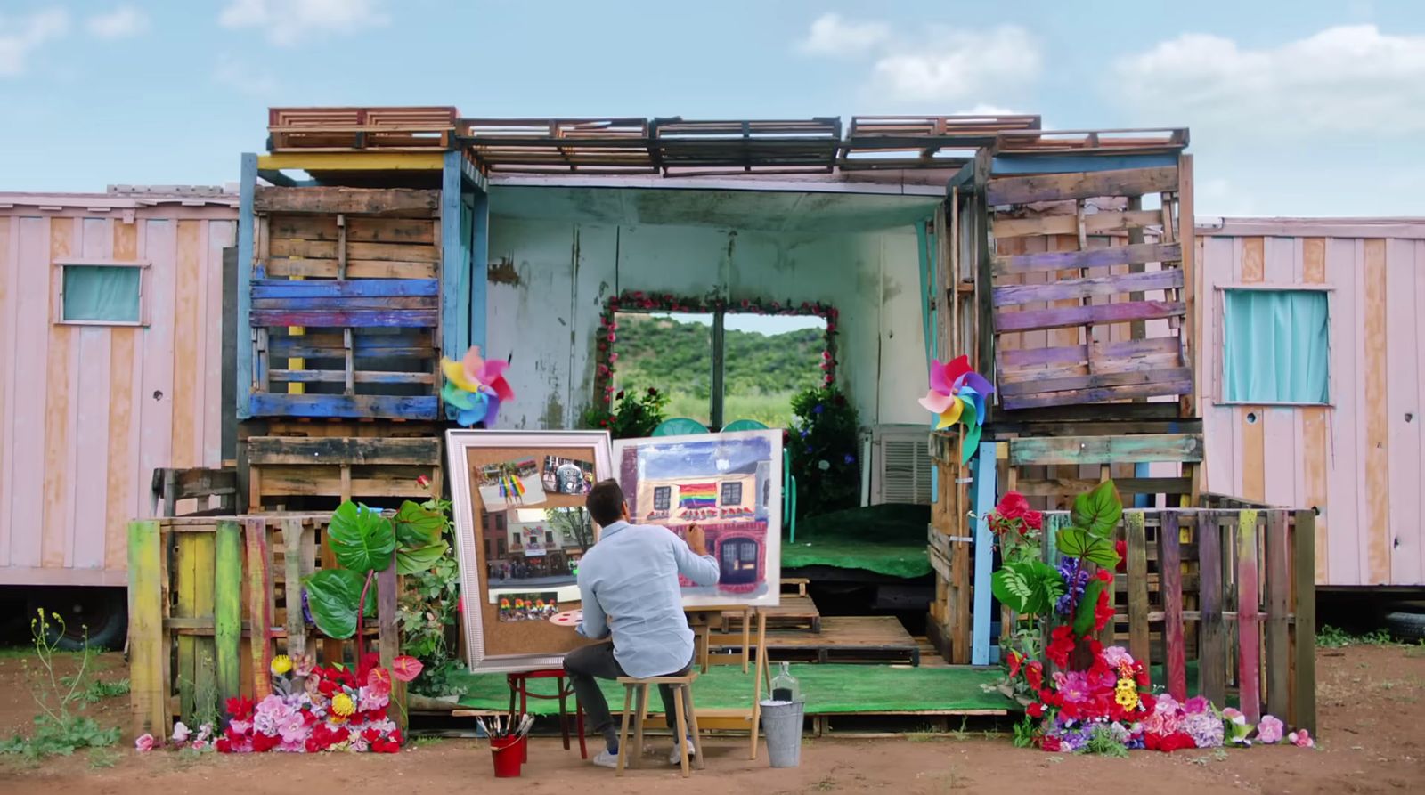a man sitting at a easel in front of a painting