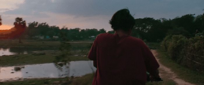 a woman walking down a dirt road next to a body of water