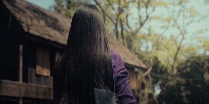 a woman with long hair walking away from a house