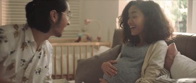 a pregnant woman sitting next to a man on a couch