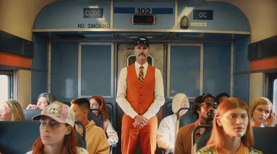 a man in an orange vest and tie standing on a train