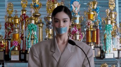 a woman wearing a mask standing in front of a wall of trophies