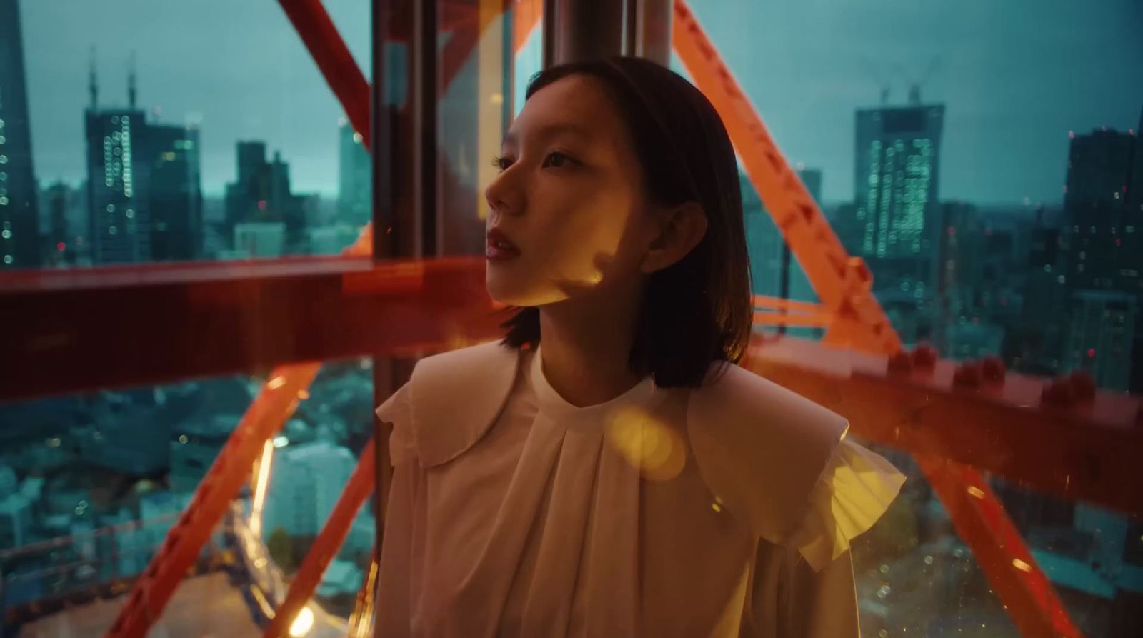 a woman standing in front of a window with a city in the background