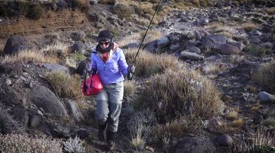 a woman walking up a hill with a fishing pole