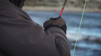 a man holding a fishing rod while standing next to a body of water