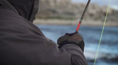 a man holding a fishing rod while standing next to a body of water