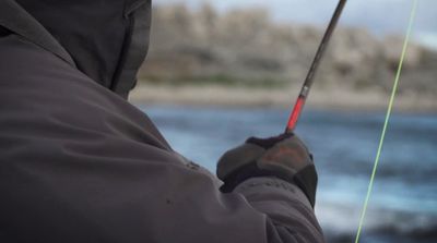 a man holding a fishing rod while standing next to a body of water