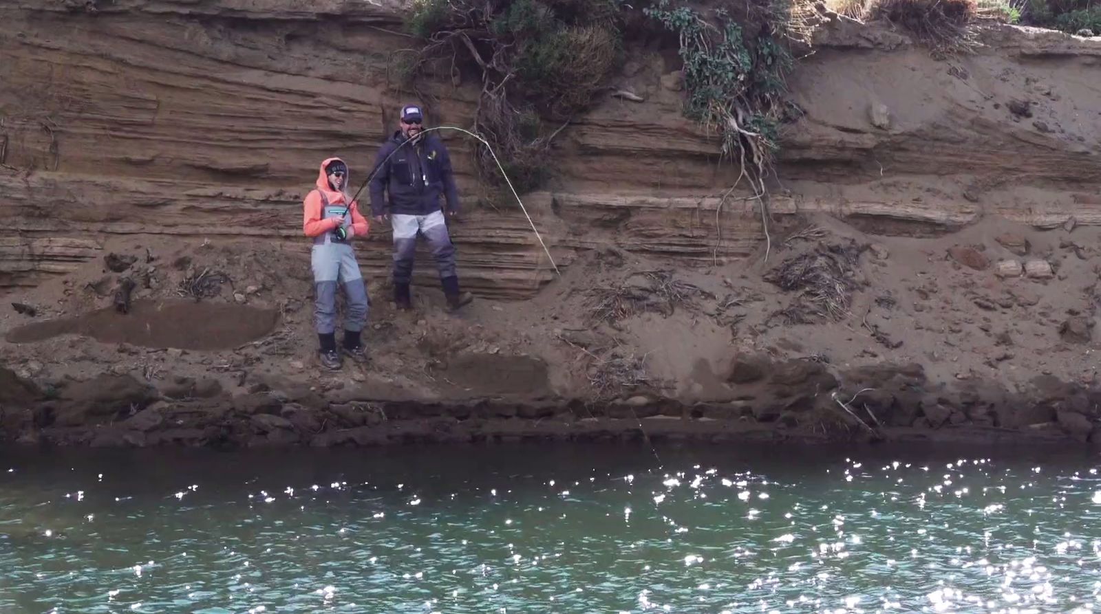 a couple of people standing on a cliff next to a body of water