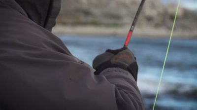 a man holding a fishing rod while standing next to a body of water